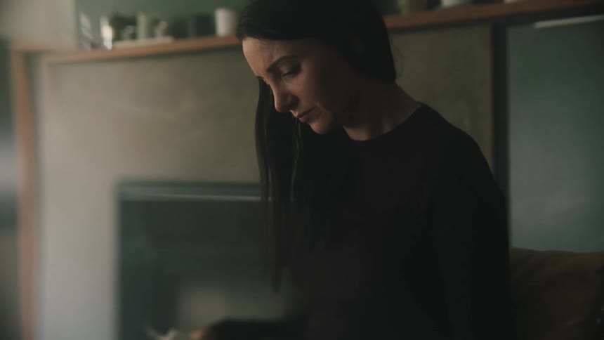 A woman sits with a worried expression looking at the papers in her hands