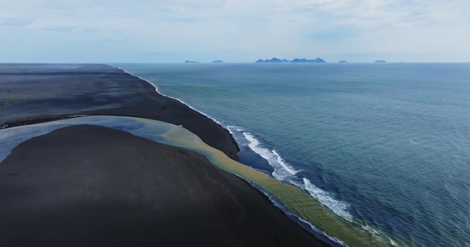 Aerial view of a blue and yellow river with a black sand beach