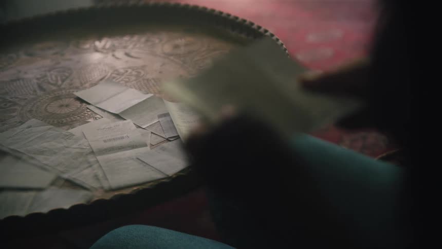 A woman is seated at a small table while she reviews and sorts receipts