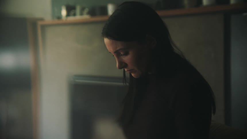 Sad woman wearing a black top looks down in the kitchen