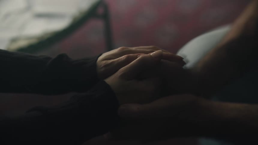 Two people hold hands and one of them makes a kindness on the others hand using their fingers