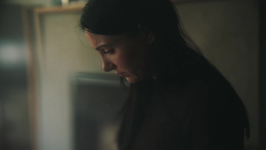 Woman sitting inside a house looking down with a sad expression on her face