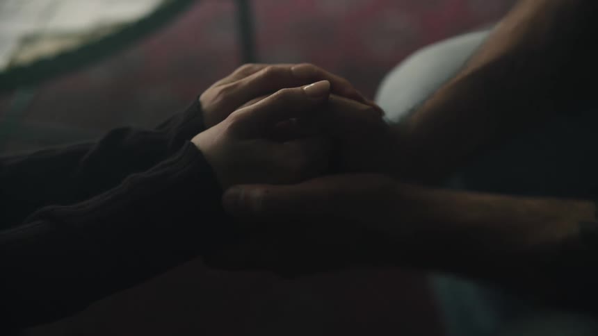 Two adult holding hands while sitting in a faintly dark room