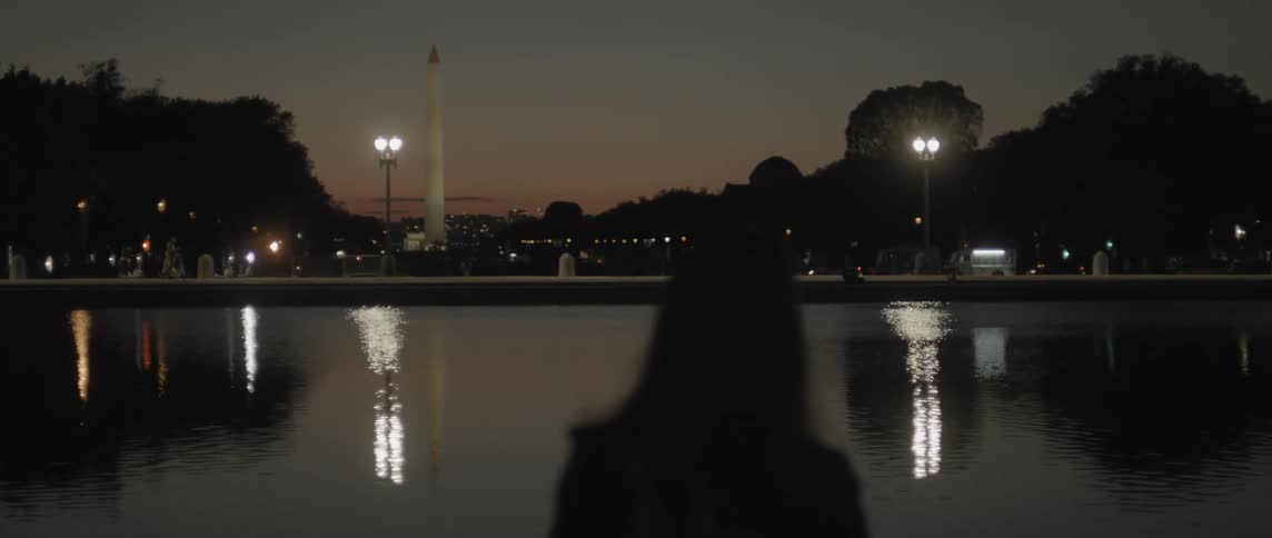 Back view of a lady standing near a river at night