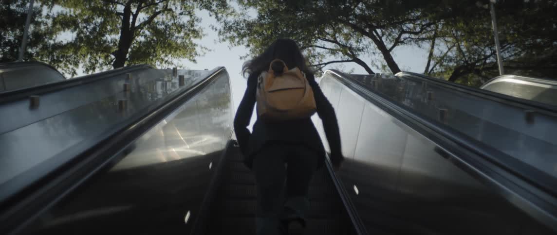 Young girl with a backpack walks on an escalator to get on the street at midday