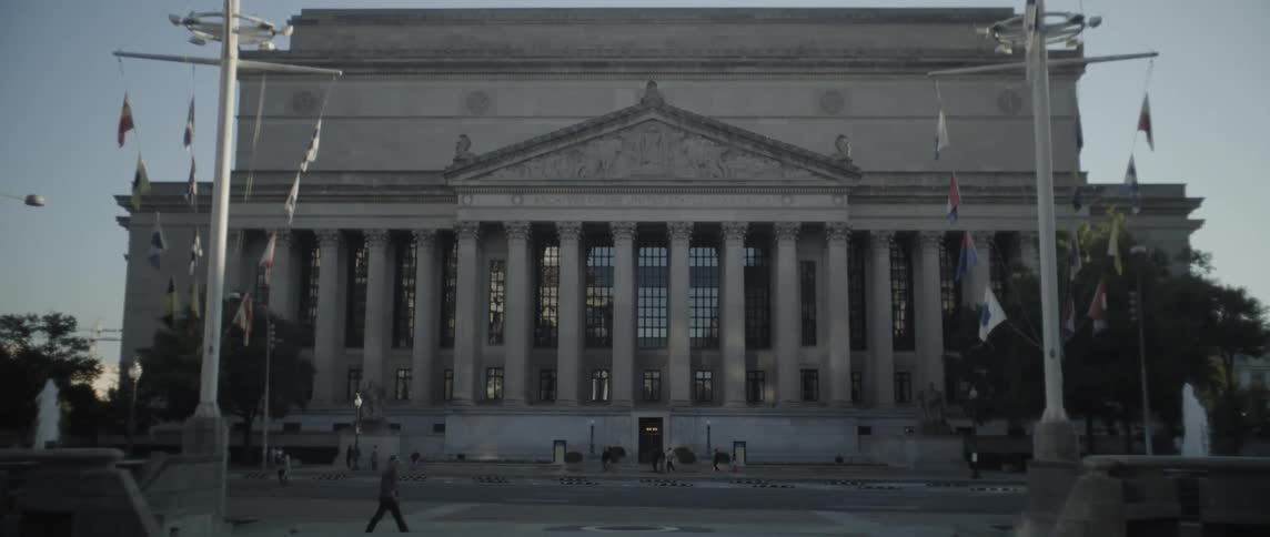Tourists walk past the building with pillars