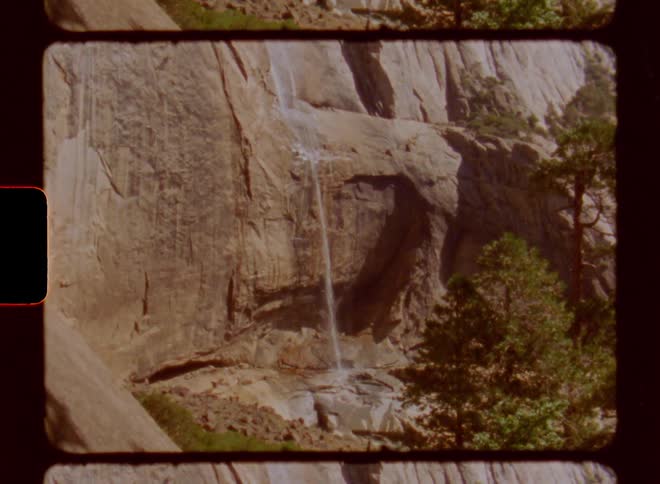 Narrow waterfall flows down cliff into pool near conifers