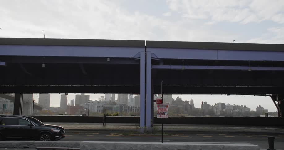 A person walking on the sidewalk under a bridge