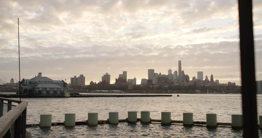 Some people walking on a sidewalk that faces the sea and behind them are several tall buildings in a city