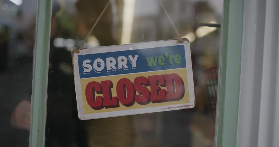 A man inside a shop turns the sign on the door from closed to open