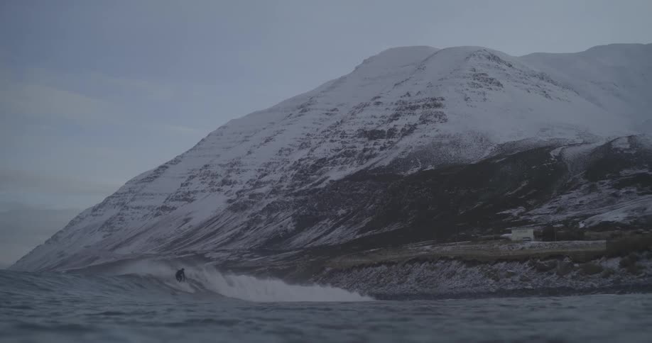 Man surfing a wave in the winter with snowcovered mountains in the background