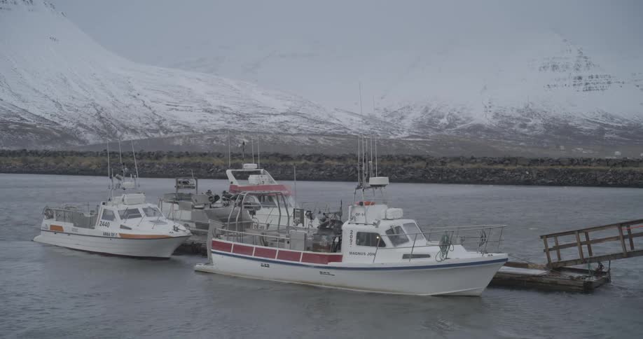 Two boats anchored in the middle of the sea with snowcovered mountains in the background