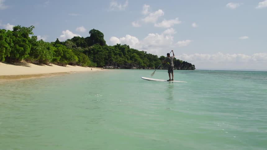 Man on paddle board paddles beside the shore