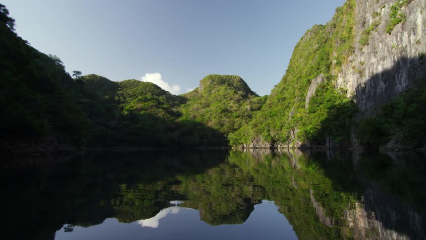 A calm body of water with tree covered mountains around it on a sunny day