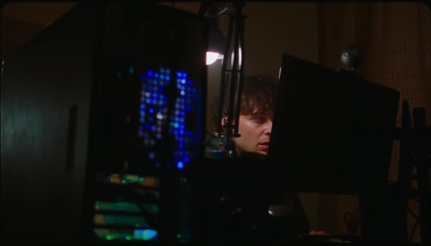 Man sitting in front of his computer in a dark room with a sleepy and cold facial expression
