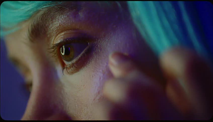Portrait of a young woman with blue hair sticking a shiny butterflyshaped gem on her face