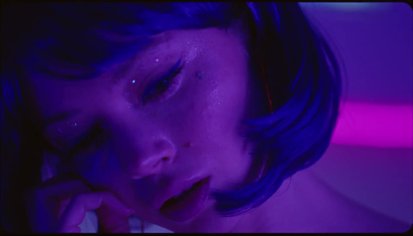 Young woman wearing a purple wig posing indoors under neon lights