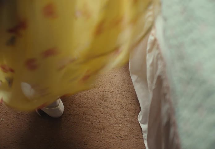 A child swirling her yellow dress beside the bed indoor