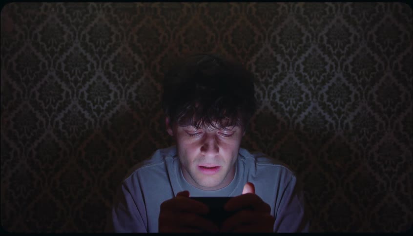 Man concentrates on the screen of a mobile phone with his back against the wall