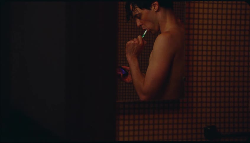 A man is looking at his phone as he brushes his teeth