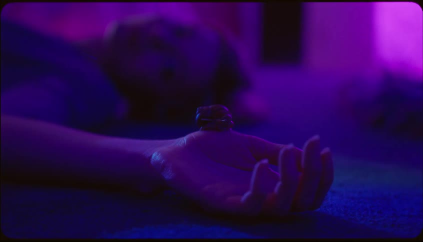 Close up of hand zooms out to female lying face up indoors under purple lighting