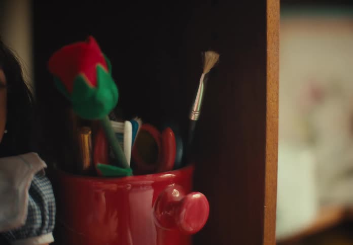 Doll sits on shelf next to cup holding pens and other items