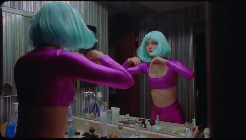 Woman puts on light blue wig while standing in front of bathroom mirror