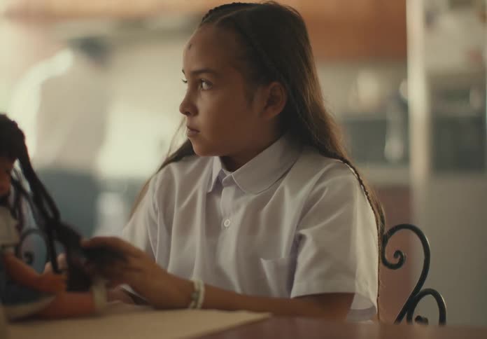 Girl braiding her dolls hair while sitting at a table
