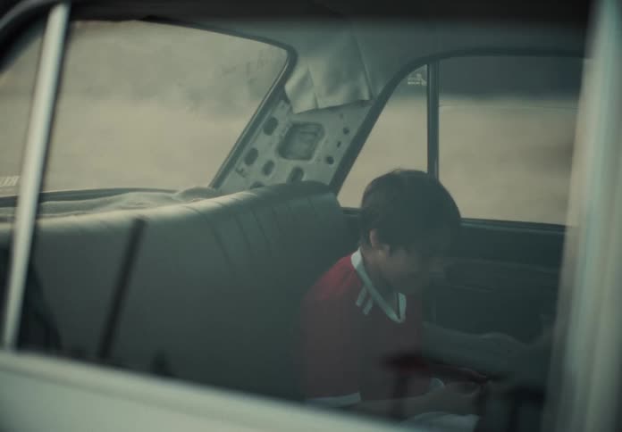 Boy wearing sports jersey cries in the backseat of car before the vehicle drives away