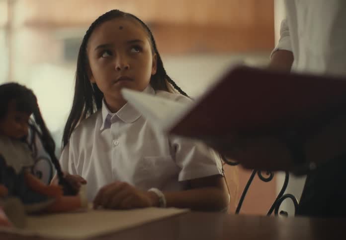 A girl playing with her doll when someone arrives asks for the book and angrily throws it on the table