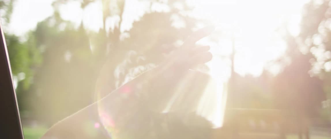 View of a womans arm out of a moving car in slow motion with a forest in the background and a sunlight reflection