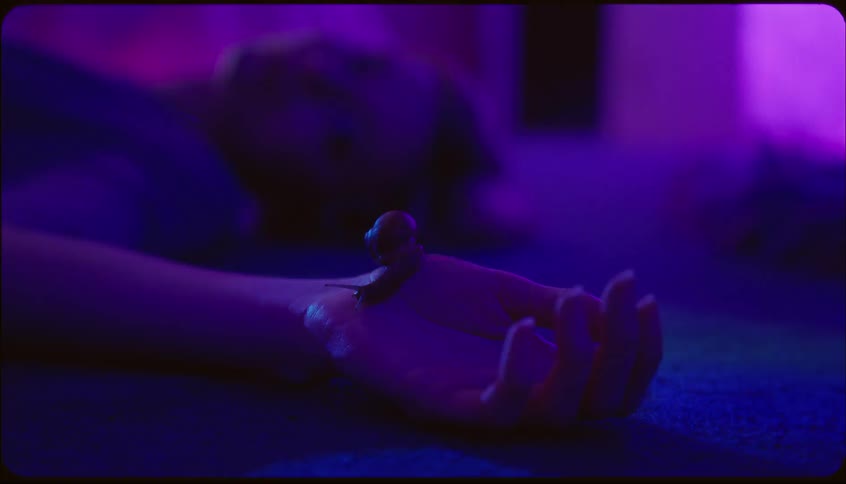 Woman lying on the floor in a purplelit environment with a slug crawling on her hand
