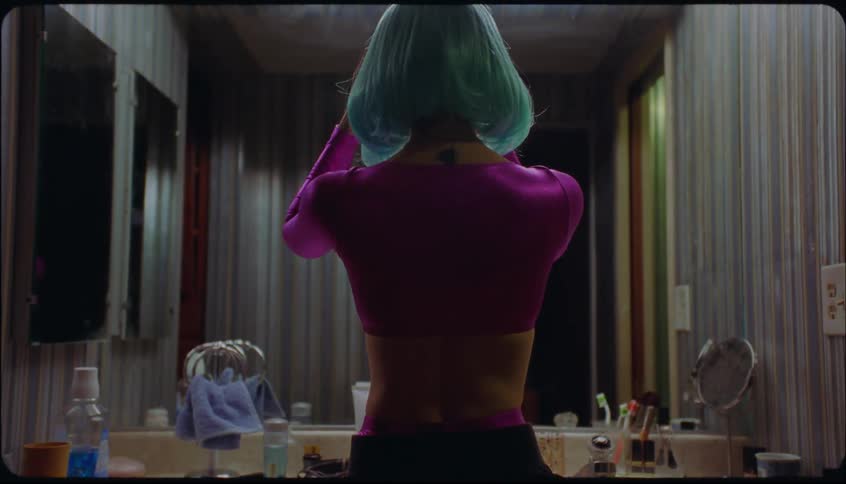 Woman adjust her blue wig while standing in front of bathroom mirror