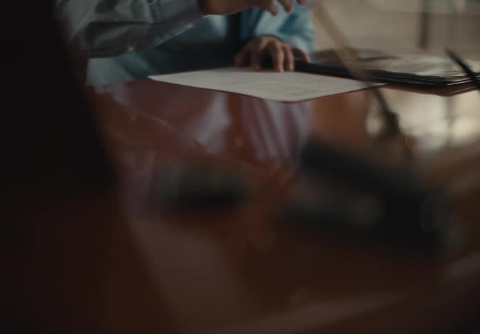 Man sitting at large wooden desk in office fills out paperwork and signs it