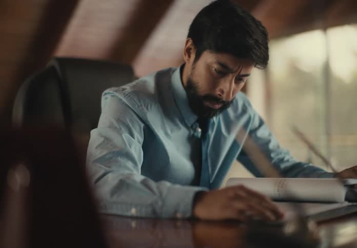 Portrait of a man sitting reading a document shaking his head in a negative gesture and displaying an angry facial expression