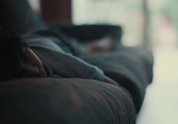 Boy lies on cushions as person walks out of house through sliding glass door