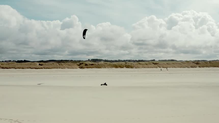 Kite drags wind powered vehicle across the sand on a cloudy day
