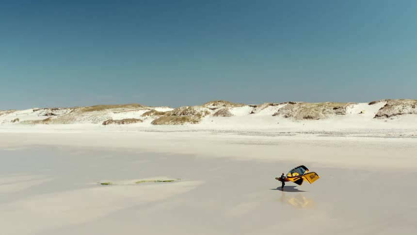 Aerial panorama of the white sandy beach with a person walking with their kitesurf