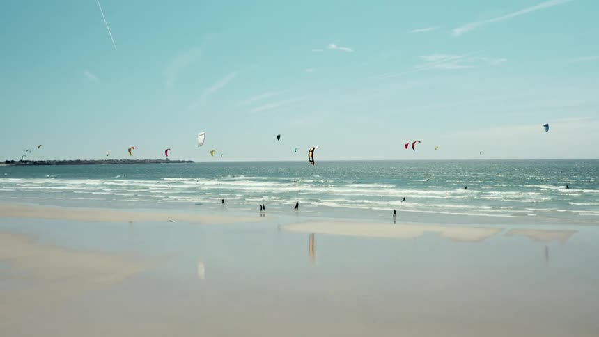 People para surf and fly kites at beach on a slightly cloudy day