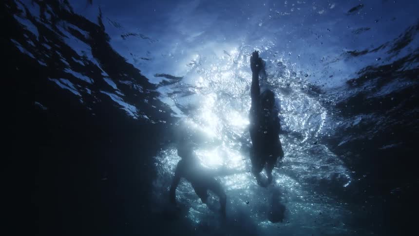 View from inside the water of two people swimming and the sunlight reflection