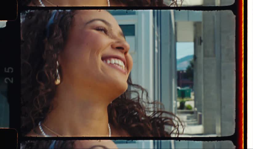 Woman smiles while standing outdoors near building columns on a sunny day