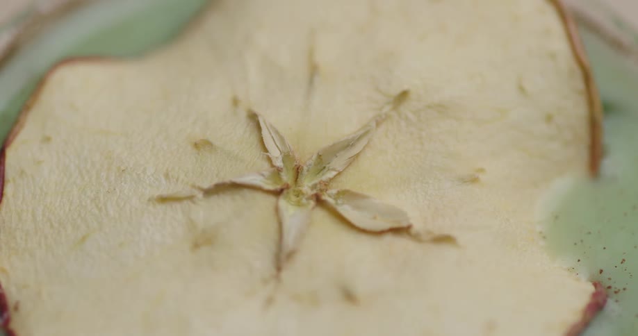 Dried apple being placed inside a glass with green liquid and ice