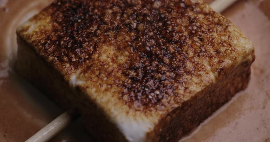 Closeup of a marshmallow in bubbling liquid chocolate changing color when roasted