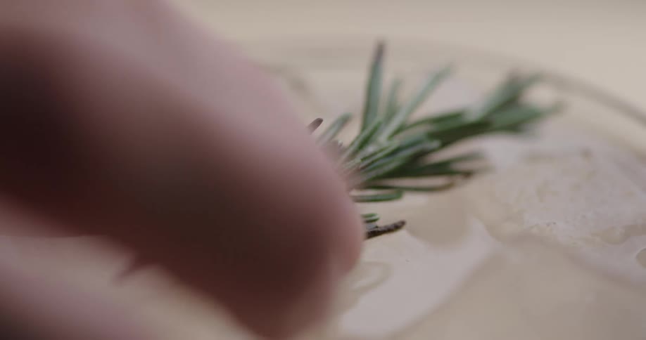 A sprig of rosemary is placed on top of some ice cubes floating in a clear beverage in a glass