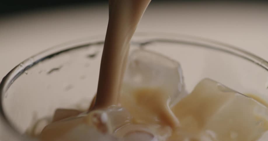 Beverage being poured from a jug into a glass cup filled with ice cubes