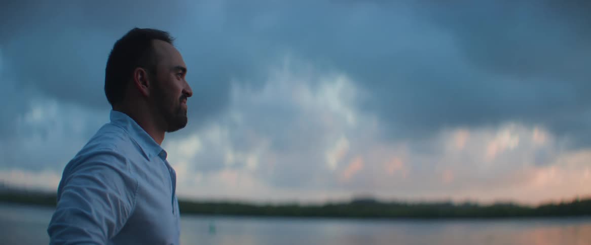 Man enjoying the view of a lake and a sunrise sky with a smiling expression