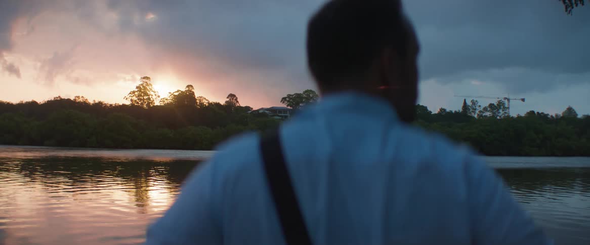 A man stands near a river looking around at dusk
