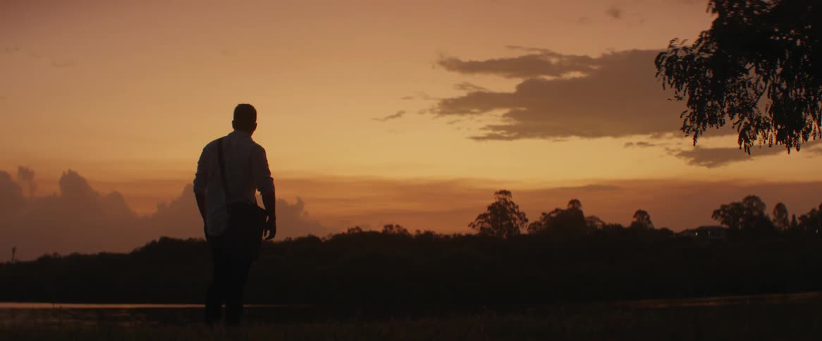 Man walks nearby a river at sunset puts both hands inside his pocket and stood still