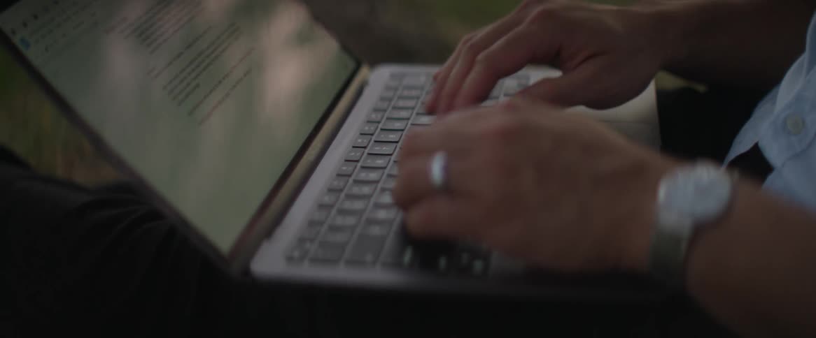 A man sitting in a park typing on his laptop