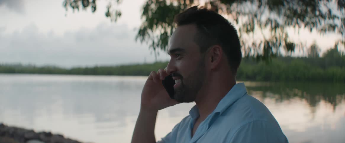 Portrait of a man talking on the phone smiling next to a lake
